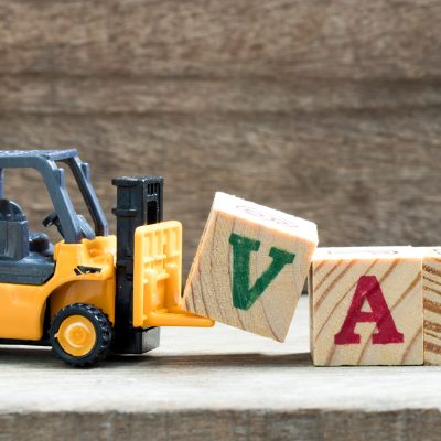 Toy plastic forklift hold block V to compose and fulfill wording VAT on wood background